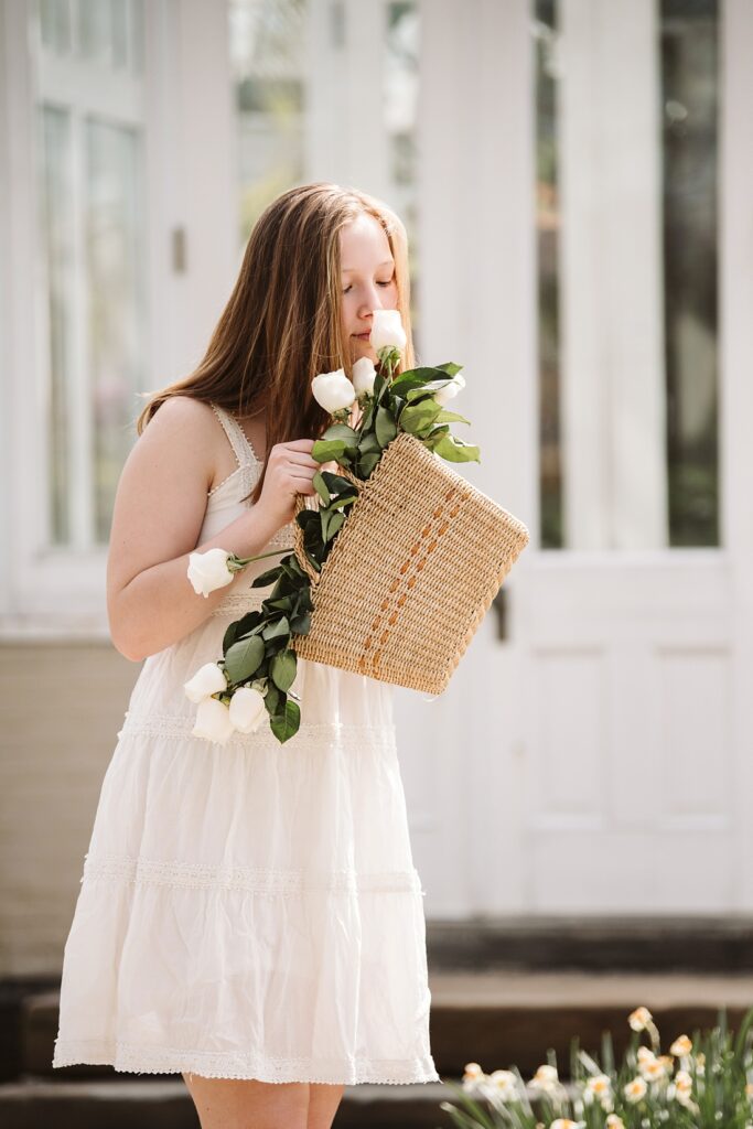 senior girl smells roses from a wicker basket near a greenhouse in Frick Park