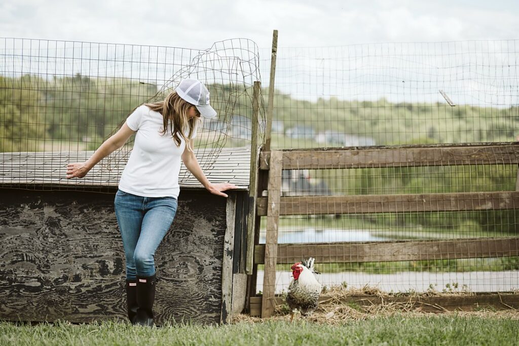 Personal branding portrait of a health coach standing near a chicken on a farm