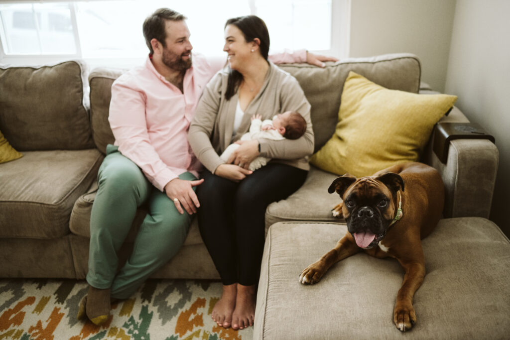 newborn lifestyle picture of family holding baby with dog in living room
