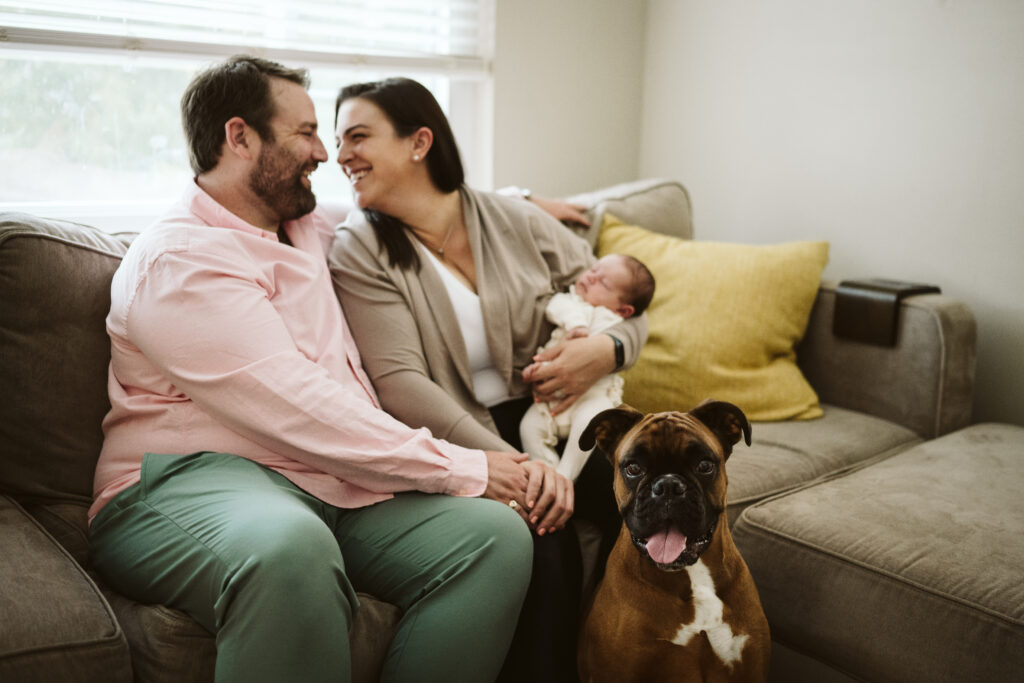 newborn lifestyle picture of family holding baby with dog in living room