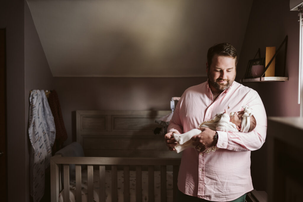 newborn lifestyle picture of a father holding baby in the nursery
