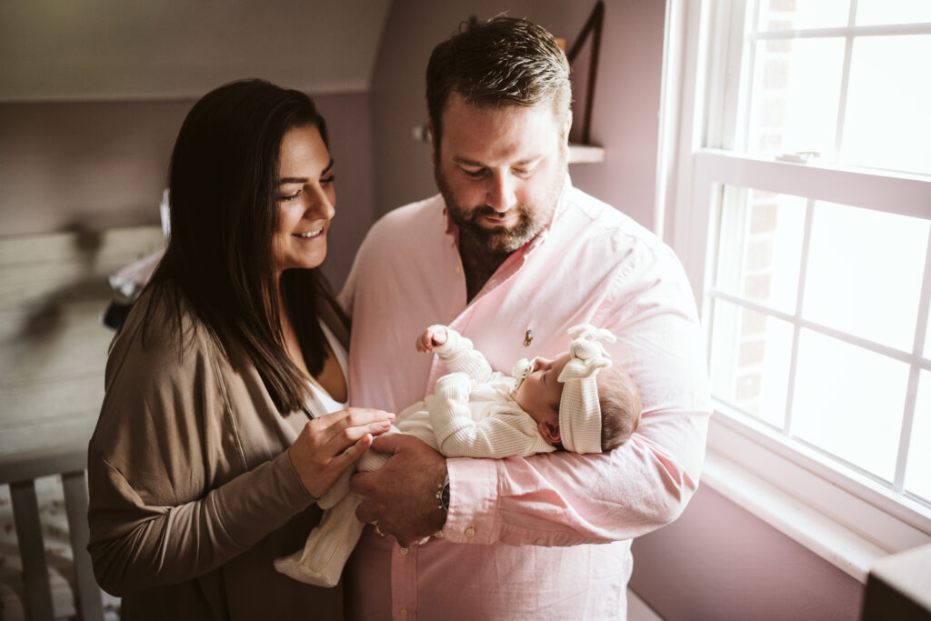 newborn lifestyle picture of family holding baby in the nursery