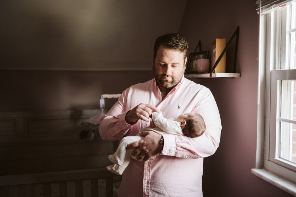 newborn lifestyle picture of a father holding baby in the nursery