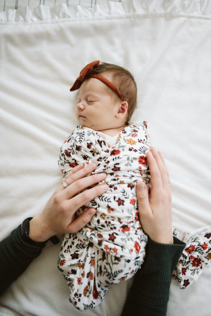 Mom swaddling newborn baby girl sleeping on bed