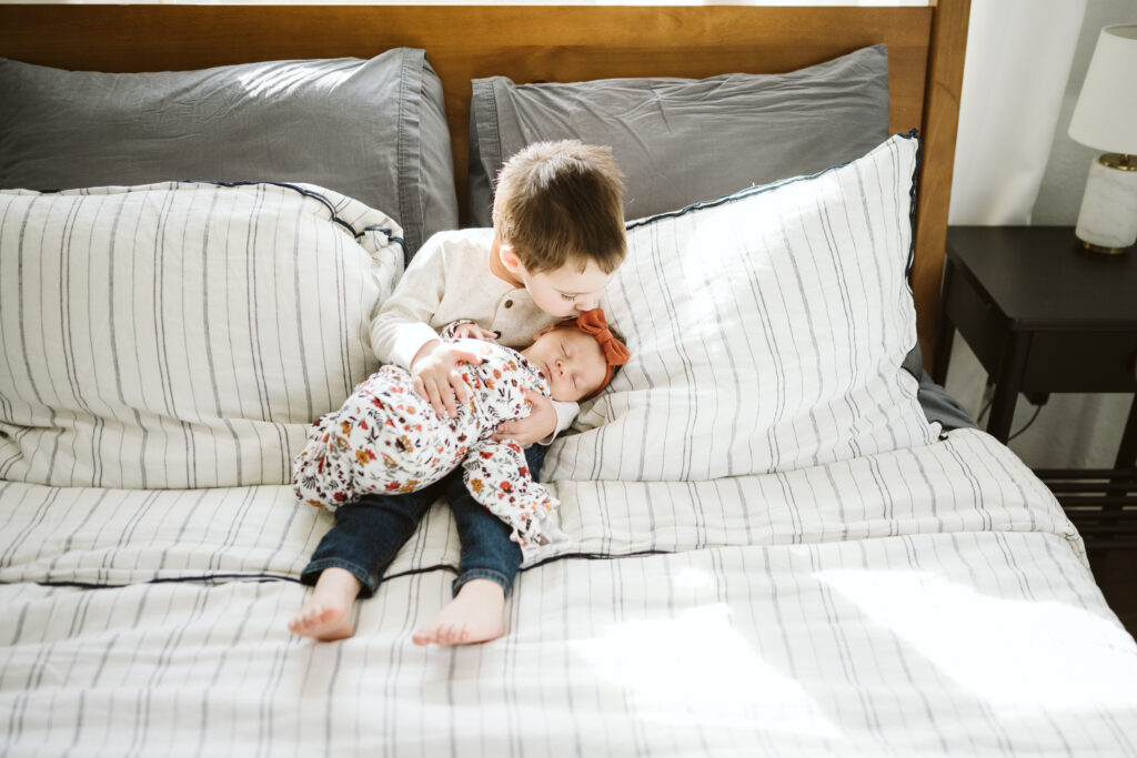 lifestyle portrait of big brother kissing baby sister
