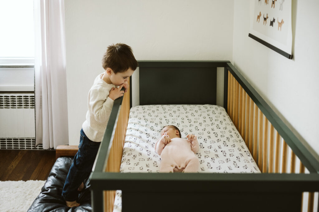 big bother looking at newborn sister sleeping in crib