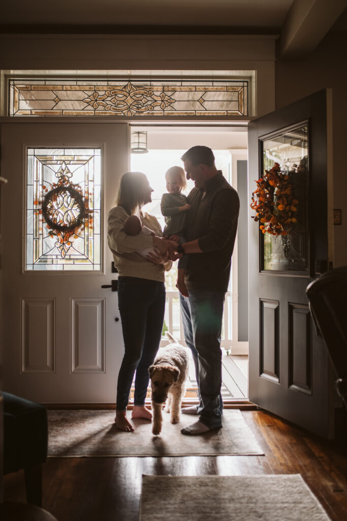 newborn lifestyle photo of family holding baby with dog at front door