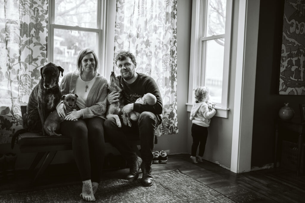 newborn lifestyle picture of family holding baby with dog at home