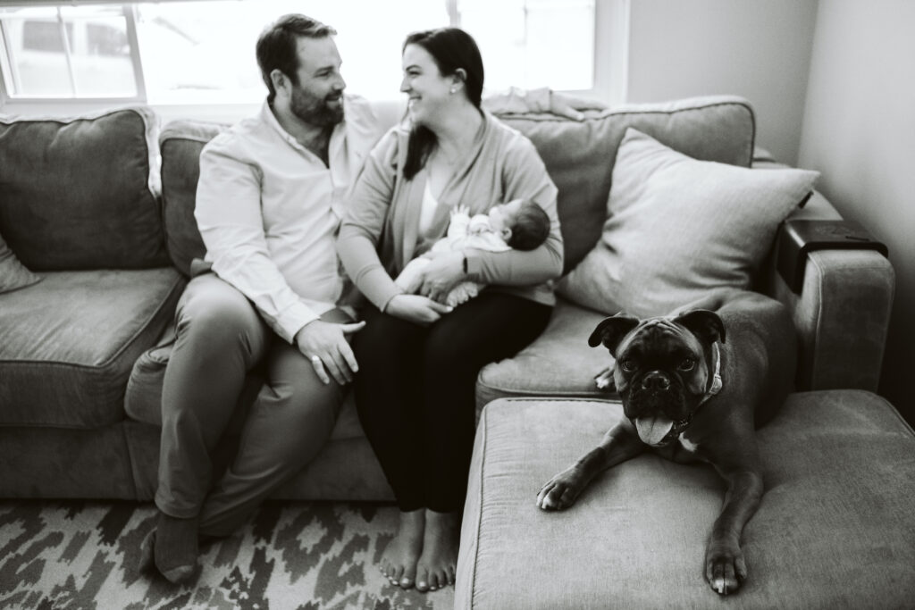 newborn lifestyle picture of family holding baby with dog in living room