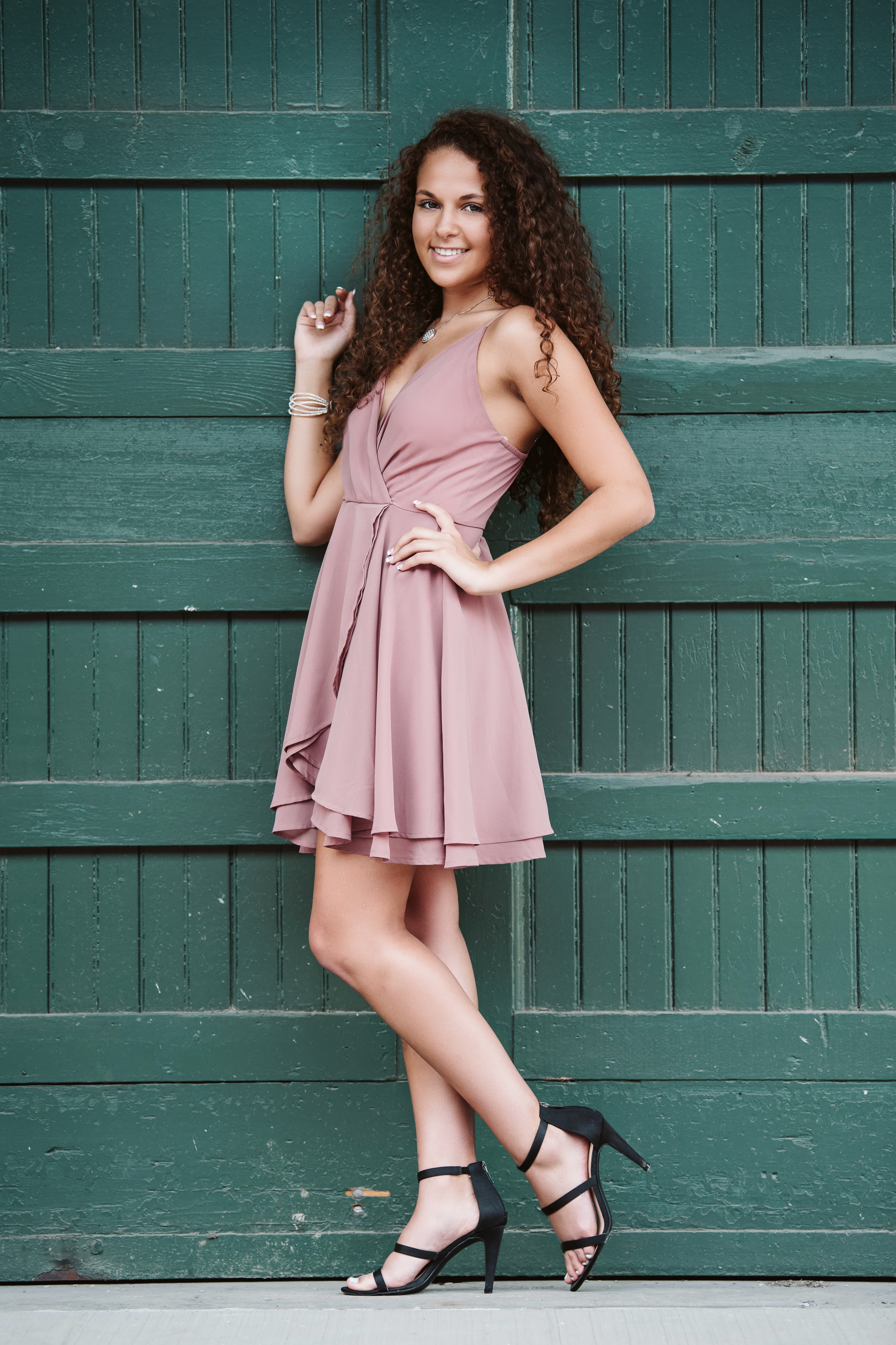 portrait of high school senior girl wearing a pink dress in front of a green wall