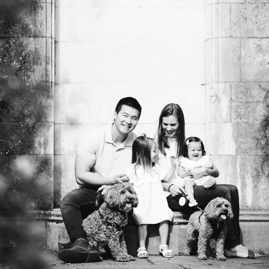 A black and white portrait of a family of three with their two doodles walking in a park near Pittsburgh. Portrait by Laura Mares Photography, Pittsburgh Family Photographer