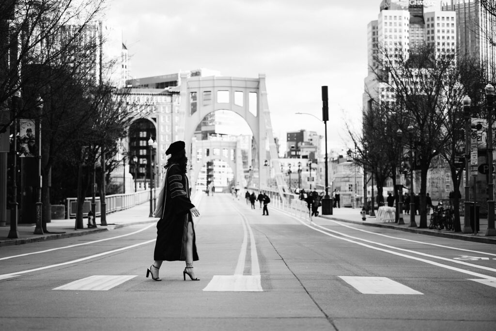 black and white senior photo of graduate walking across the street in Pittsburgh