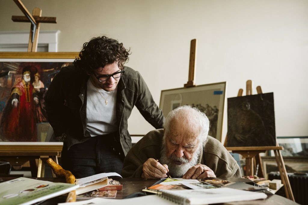 John Del Monte with his grandson in his art studio filled with paintings