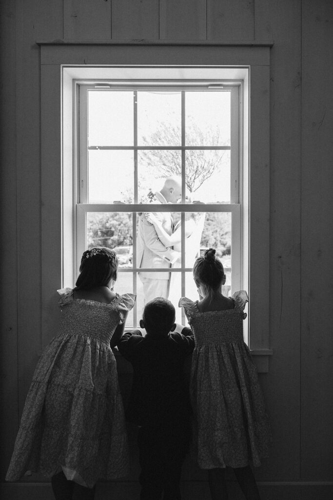 Grayson House wedding bride and groom kissing outside while kids watch from inside