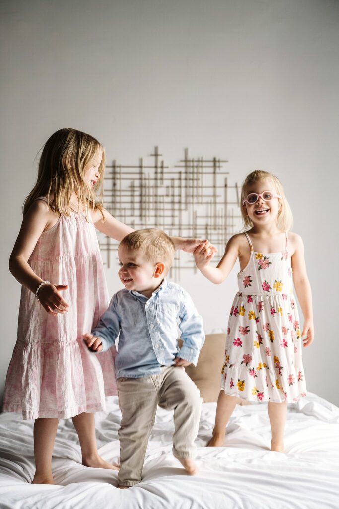 big siblings jumping on bed during newborn photoshoot