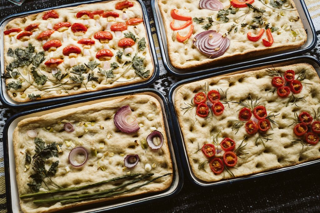 focaccia bread decorated with tomatoes, onions, garlic, asparagus, peppers, and fresh herbs