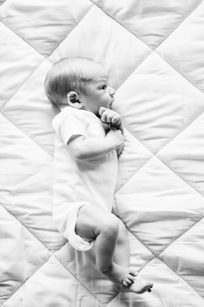 black and white natural portrait of newborn baby laying on white bed in white studio