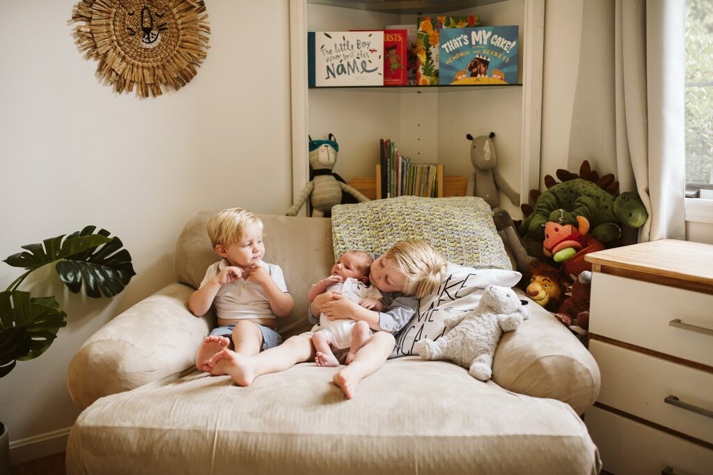 lifestyle portrait of a newborn with big brothers in bedroom