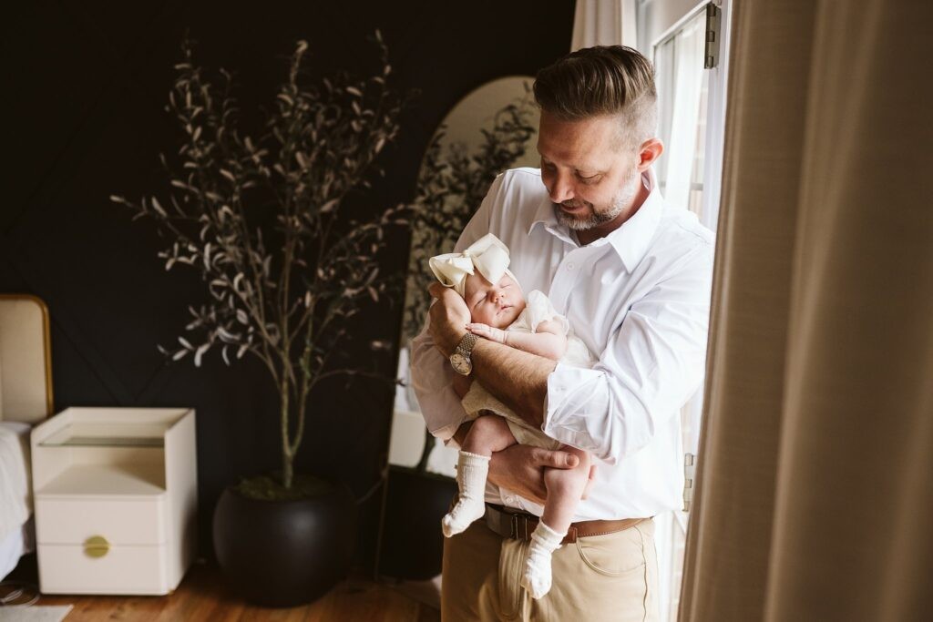 dad holding newborn in window light