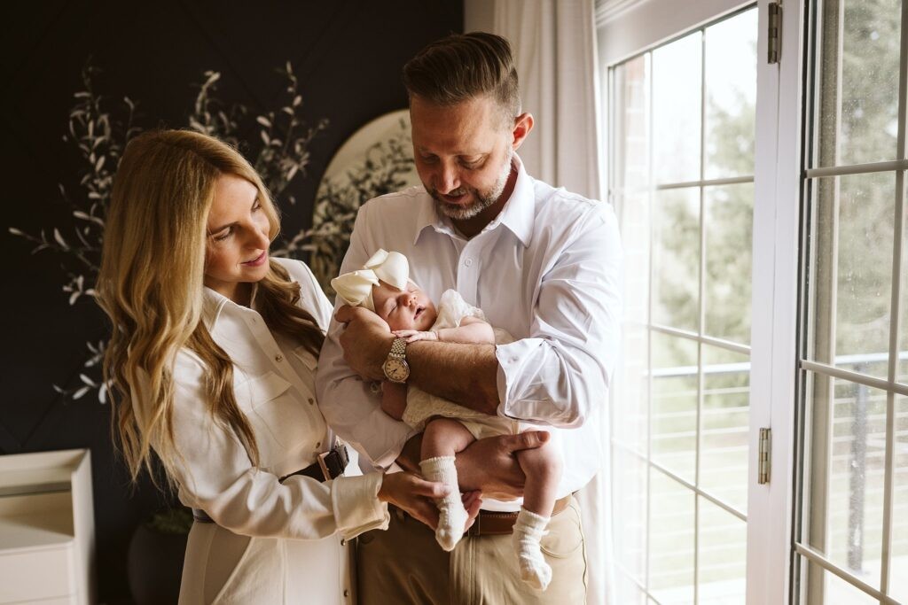 parents holding newborn in window light