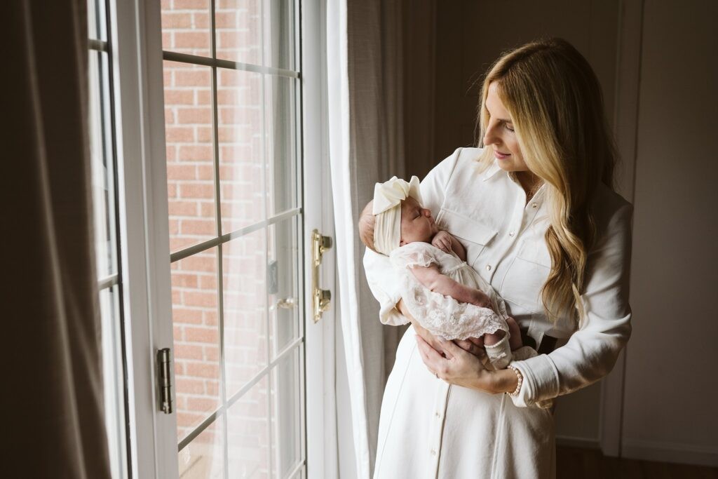 mom holding newborn in window light