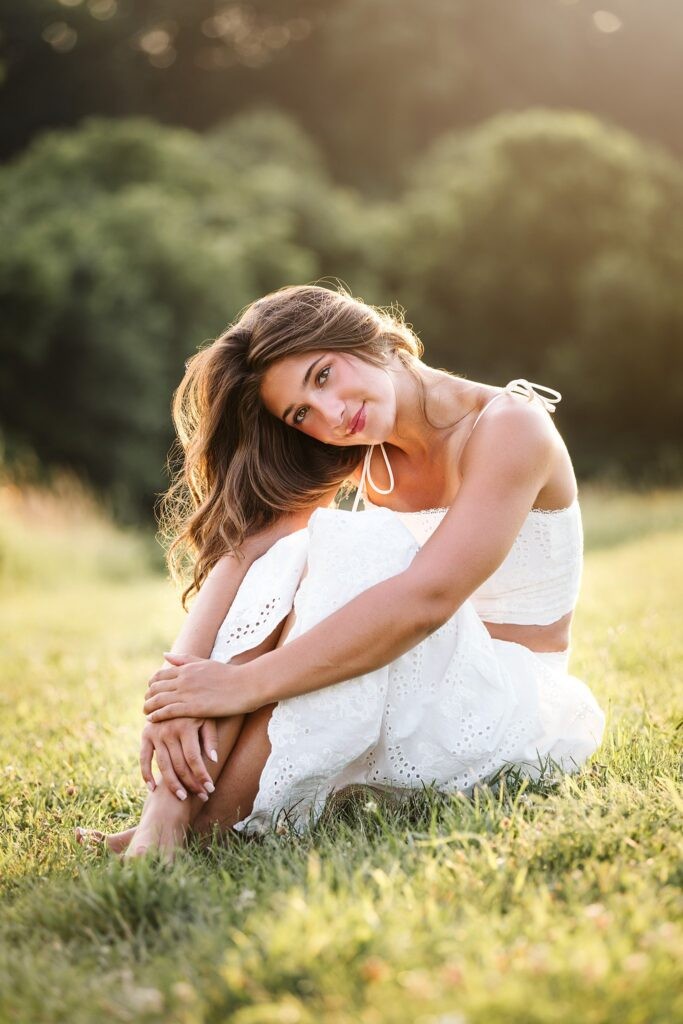 High school senior girl sitting in a field in golden hour light