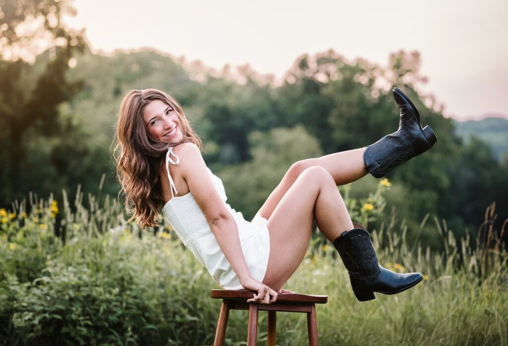 High school senior girl kicking legs while sitting on a stool in golden hour light