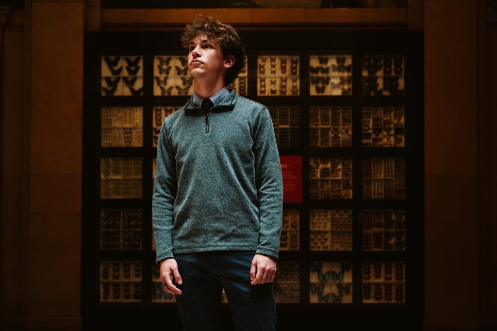 High school senior guy standing between historic museum pillars in Pittsburgh, captured in a moody and modern photography style
