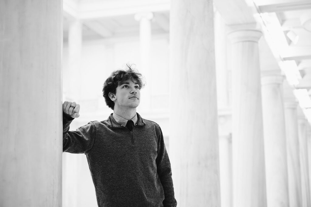 High school senior guy standing between historic museum pillars in Pittsburgh, captured in a moody and modern photography style