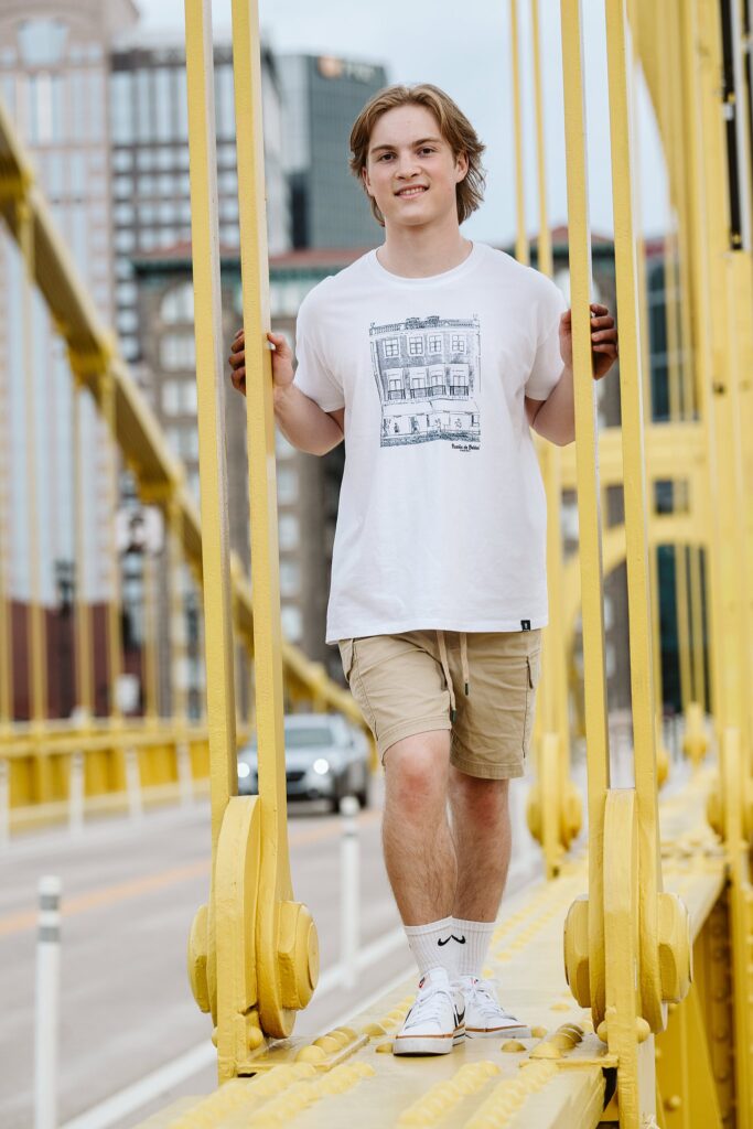 Artistic senior portraits for a guy sitting on the Roberto Clemente Bridge, featuring the yellow steel architecture and a casual, down-to-earth Pittsburgh vibe.