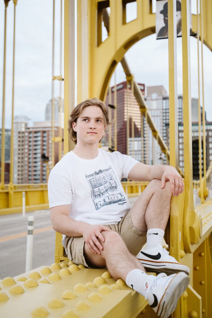 Artistic senior portraits for a guy sitting on the Roberto Clemente Bridge, featuring the yellow steel architecture and a casual, down-to-earth Pittsburgh vibe.